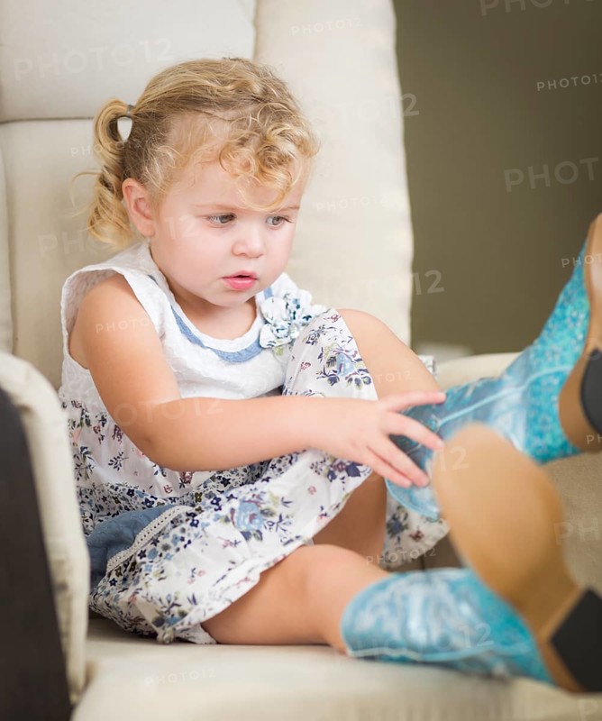 Adorable blonde haired blue eyed little girl putting on cowboy boots