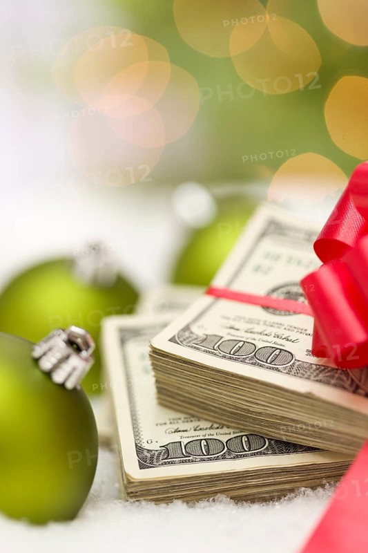 Stack of one hundred dollar bills with red bow near green christmas ornaments on snow flakes