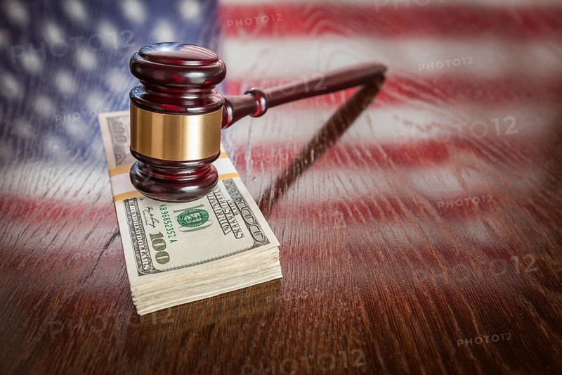 Wooden gavel resting on stack of money with american flag reflection on table