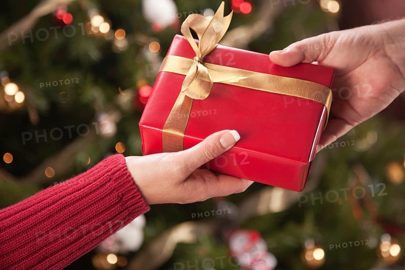 Man and woman gift exchange in front of decorated christmas tree
