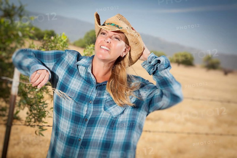 Beautiful cowgirl against barbed wire fence in field