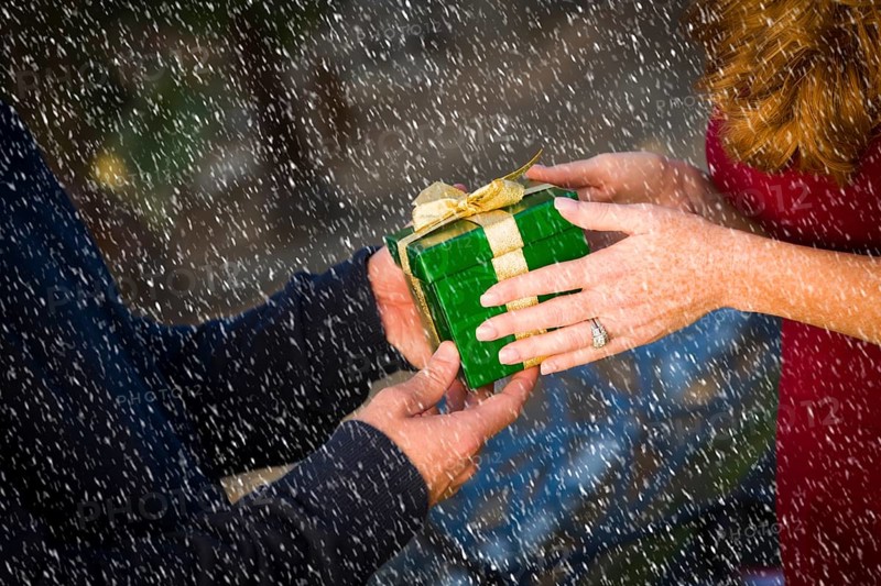 Hands of man and woman exchanging a wrapped christmas gift in the snow