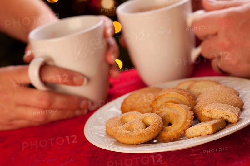 Man and woman sharing hot chocolate and cookies in front of holiday lights