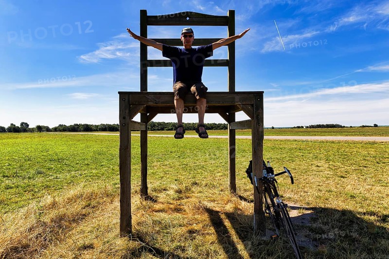 Cyclist sits on oversized chair in a meadow
