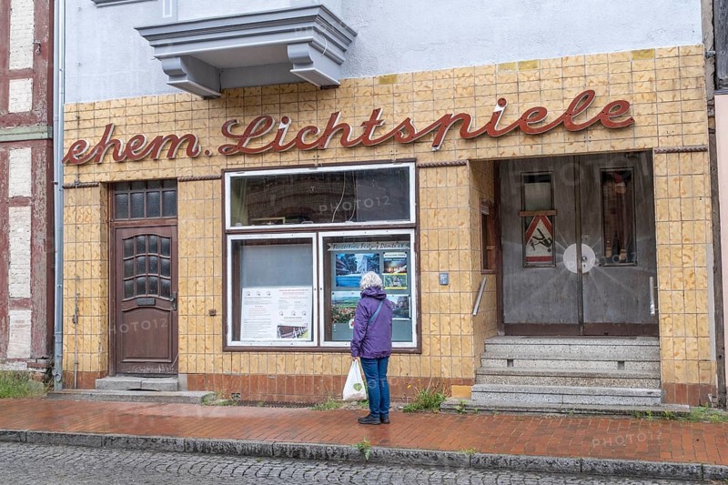 A woman stands in front of the shop window of the former cinema in Doemitz