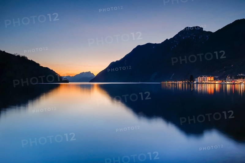 Illuminated lakeside promenade of Brunnen and view over Lake Lucerne at sunset with Mount Pilatus in the background