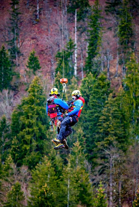 Two flight rescuers of the Bergwacht Bayern hang in the air on a wire rope