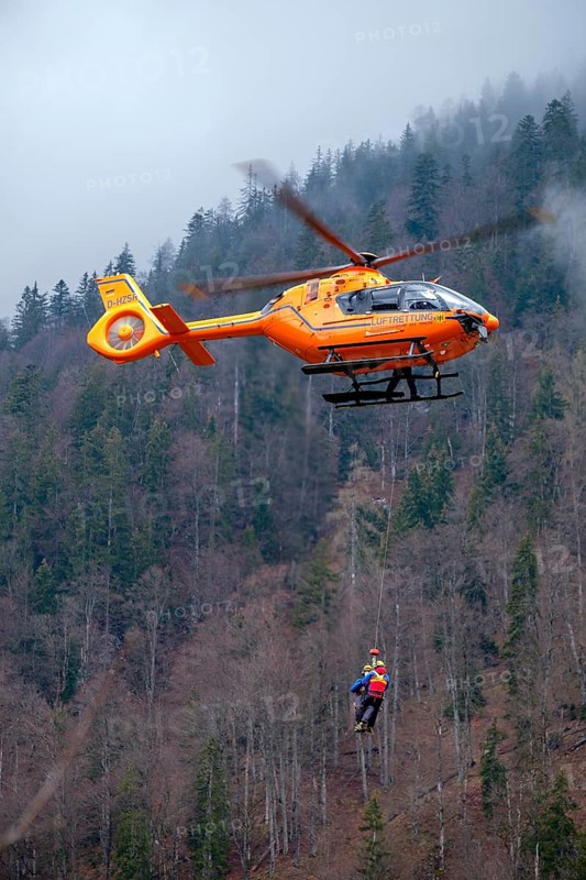 Two flight rescuers of the Bavarian Mountain Rescue Service hang on the wire rope of the rescue helicopter Christoph 14