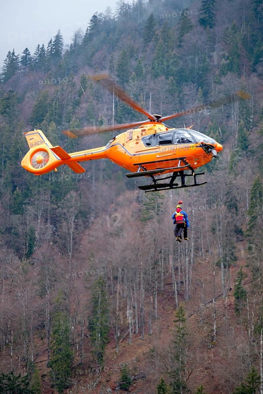 Two flight rescuers of the Bavarian Mountain Rescue Service hang on the wire rope of the rescue helicopter Christoph 14