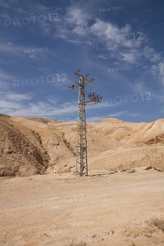 High-voltage pylon in front of mountain range with blue sky in Negev desert