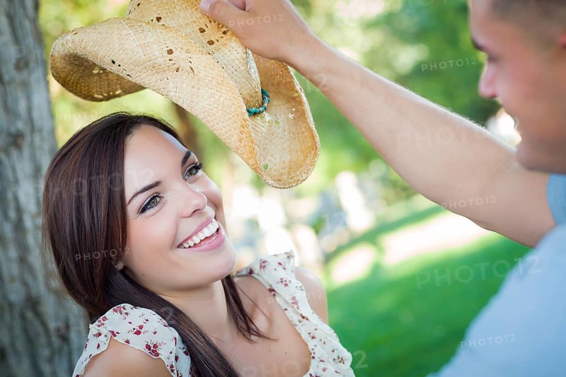 Happy mixed-race romantic couple with cowboy hat flirting in the park
