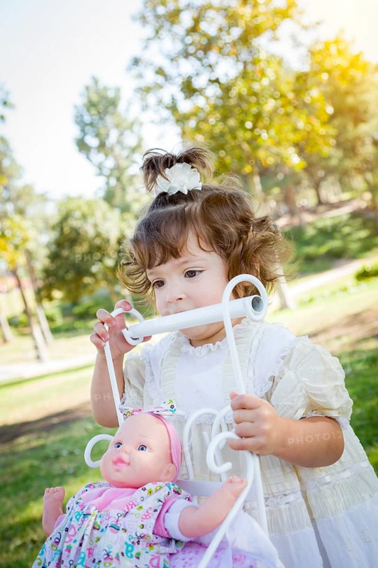 Adorable young baby girl playing with her baby doll and carriage outdoors