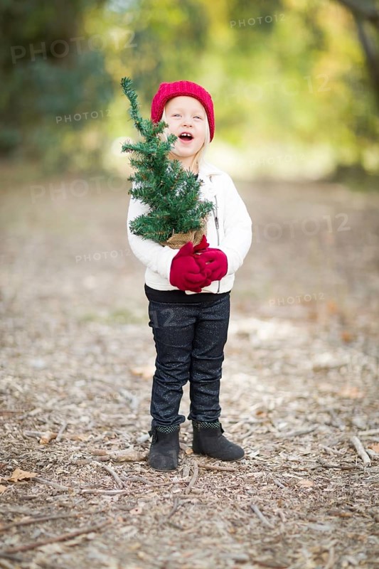 Baby girl in red mittens and cap holding small christmas tree outdoors