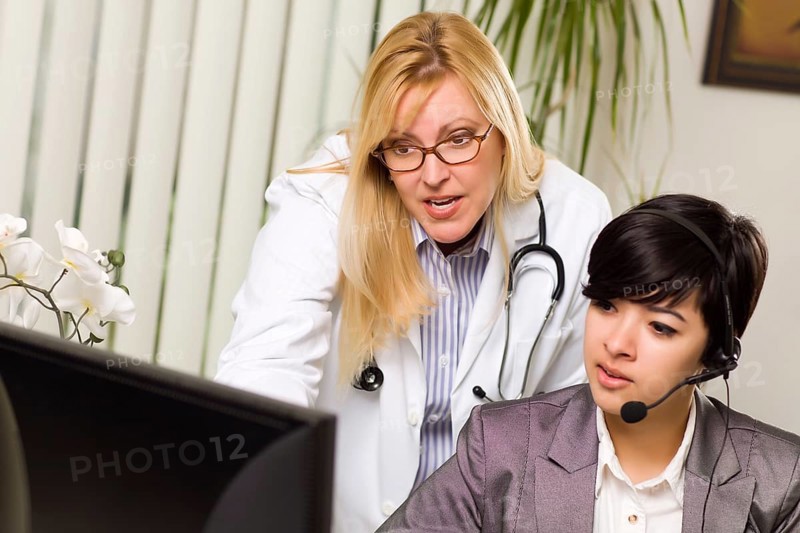 Female doctor discusses work on computer with receptionist assistant in an office setting