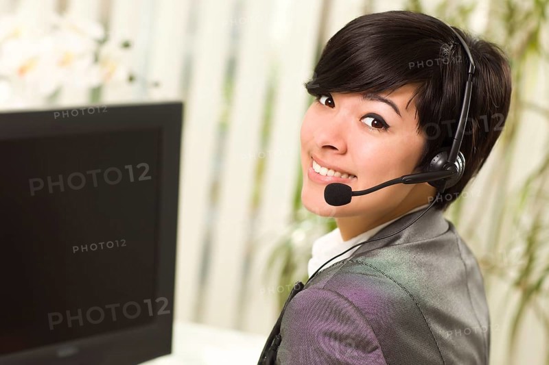 Attractive young woman smiles wearing headset near her computer monitor