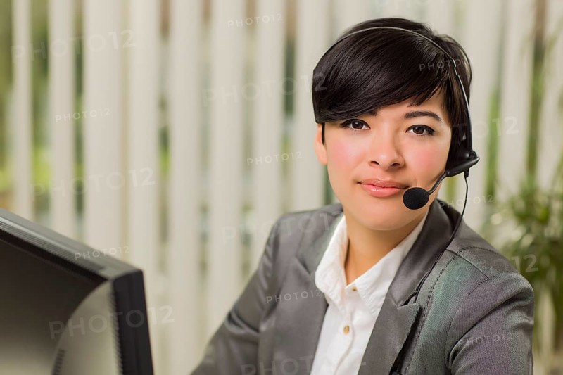 Attractive young mixed-race woman smiles wearing headset near computer monitor