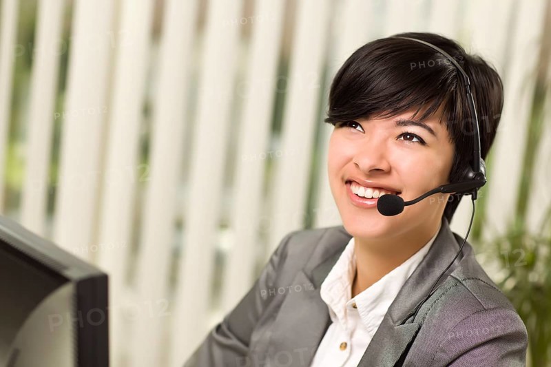 Attractive young woman smiles wearing headset near her computer monitor