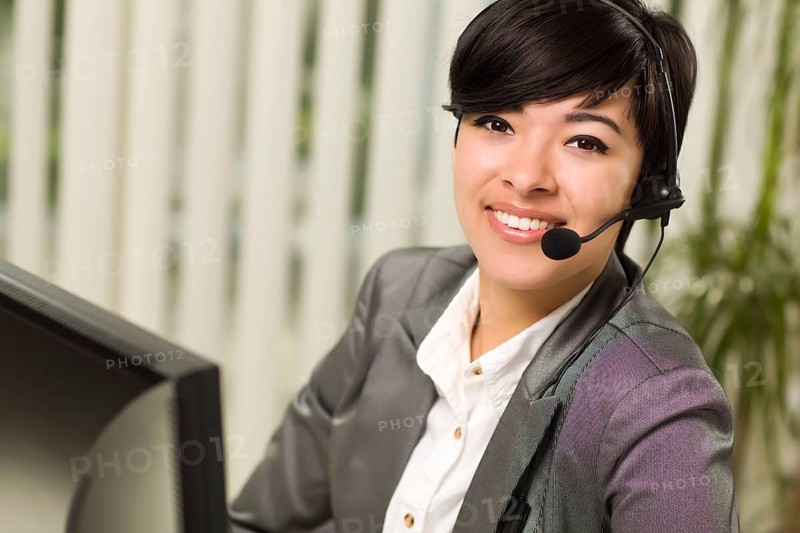 Attractive young woman smiles wearing headset near her computer monitor