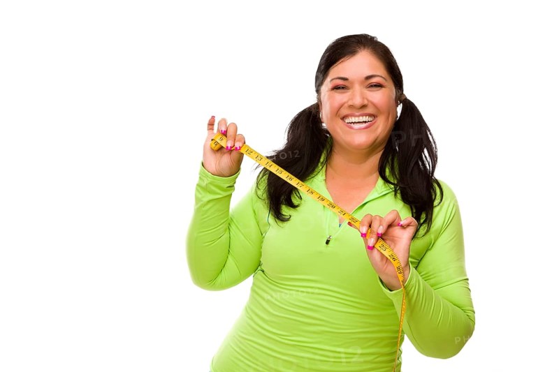 Attractive middle aged hispanic woman in workout clothes showing off her tape measure against a white background