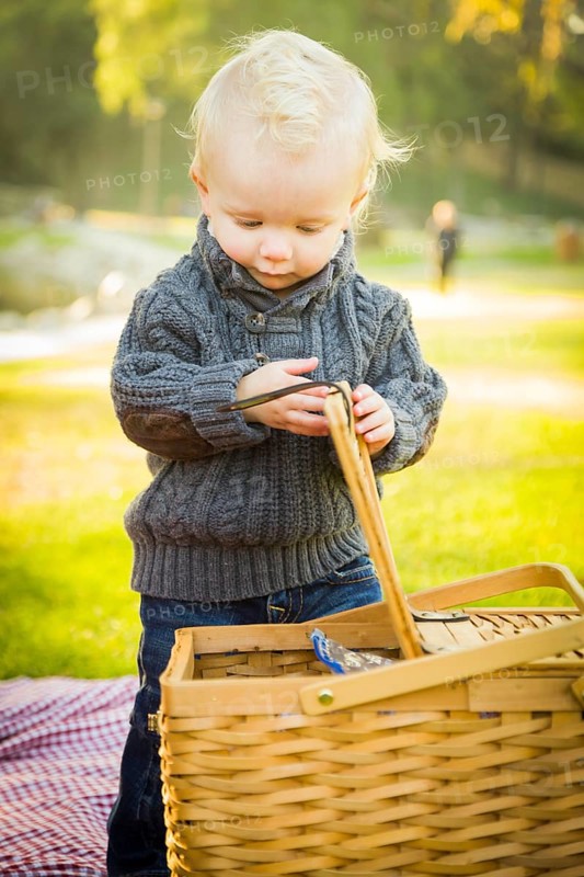 Adorable little blonde baby boy opening a picnic basket outdoors at the park