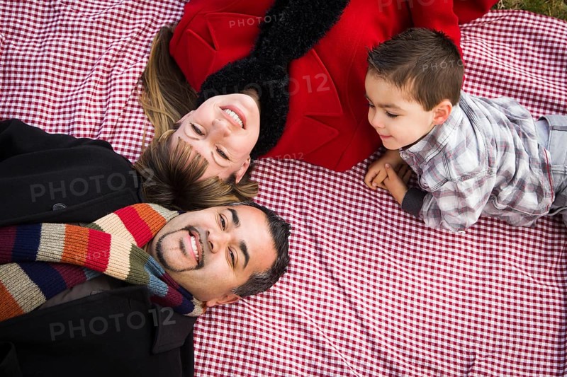 Young mixed-race family in winter clothing laying on their backs on picnic blanket in the park together