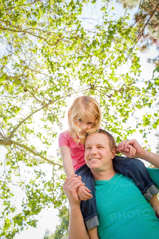 Cute young girl rides piggyback on her dads shoulders outside at the park