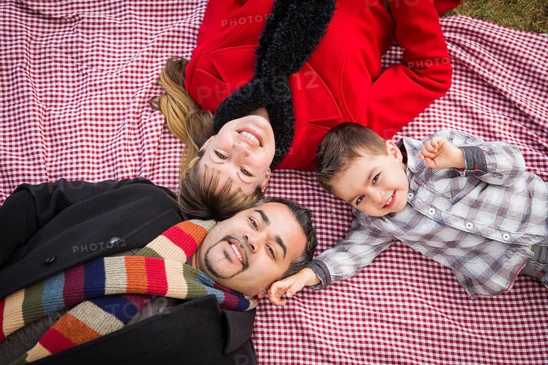 Young mixed-race family in winter clothing laying on their backs on picnic blanket in the park together