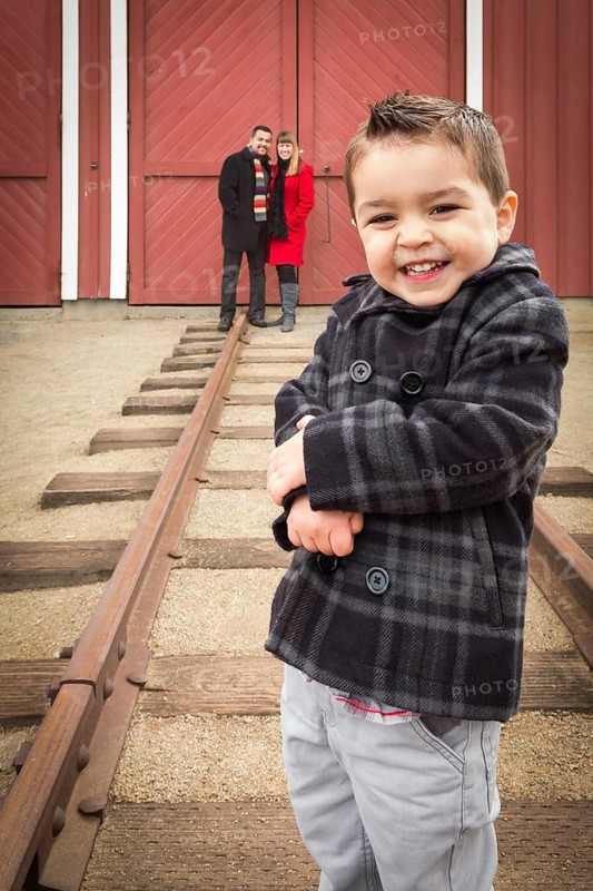 Young adorable mixed-race boy at train depot with parents smiling behind