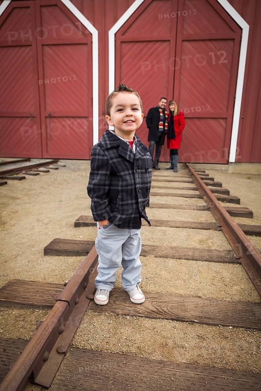 Young adorable mixed-race boy at train depot with parents smiling behind