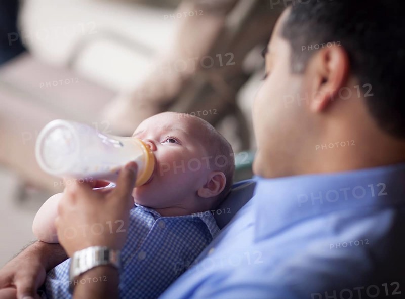 Happy hispanic father bottle feeding his very content mixed-race son