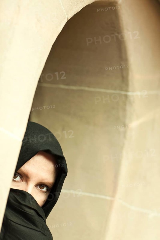 Cautious islamic woman in a window pane wearing traditional burqa or niqab