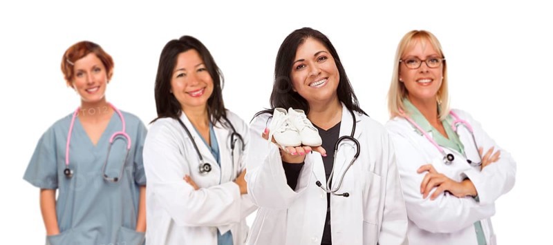 Attractive hispanic female doctor or nurse holding out baby shoes and support staff behind isolated on a white background