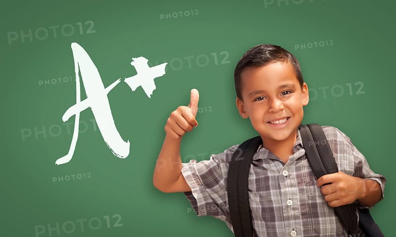 Cute hispanic boy with thumbs up in front of A+ written on chalk board