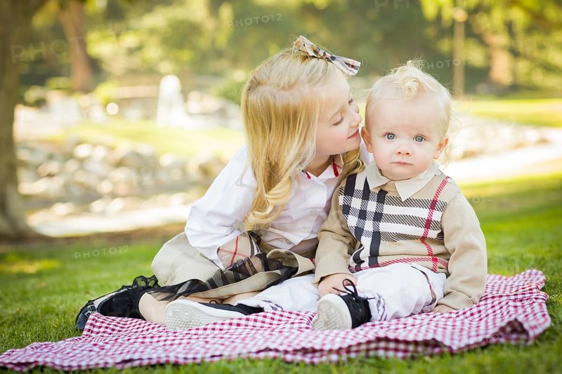 Sweet little girl kisses her baby brother on his cheek outdoors at the park