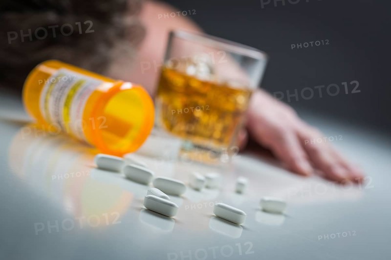 Unconscious man face down behind scattered prescription drugs and glass of alcohol