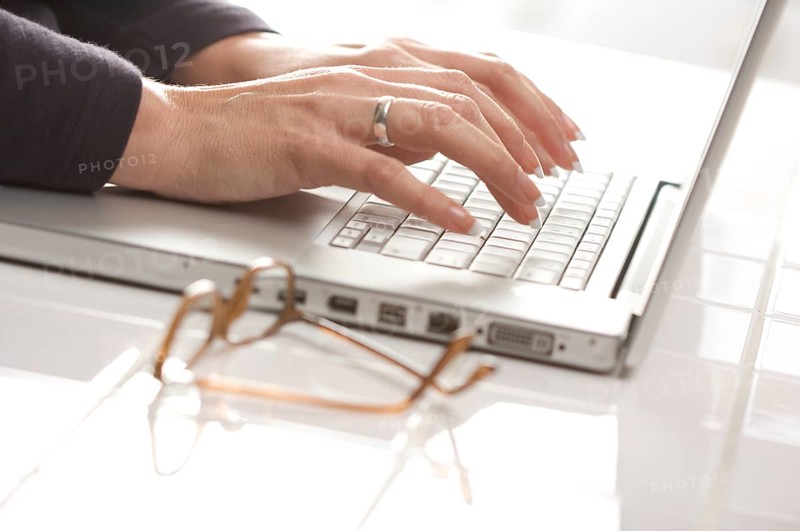 Female hands typing on the keyboard of the laptop with eyeglasses nearby