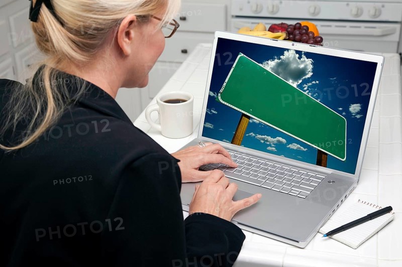 Woman in kitchen using laptop with blank road sign ready for your own message. screen can be easily used for your own message or picture. picture on screen is my copyright as well