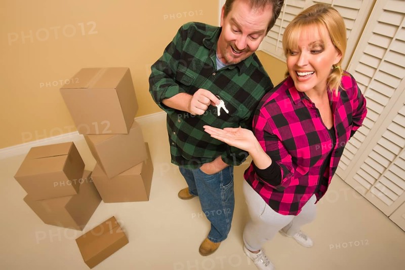Goofy excited man handing keys to smiling wife in room with packed boxes