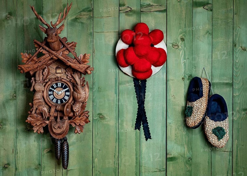 Black Forest cuckoo clock with Bollen hat and straw shoes in front of green wooden wall