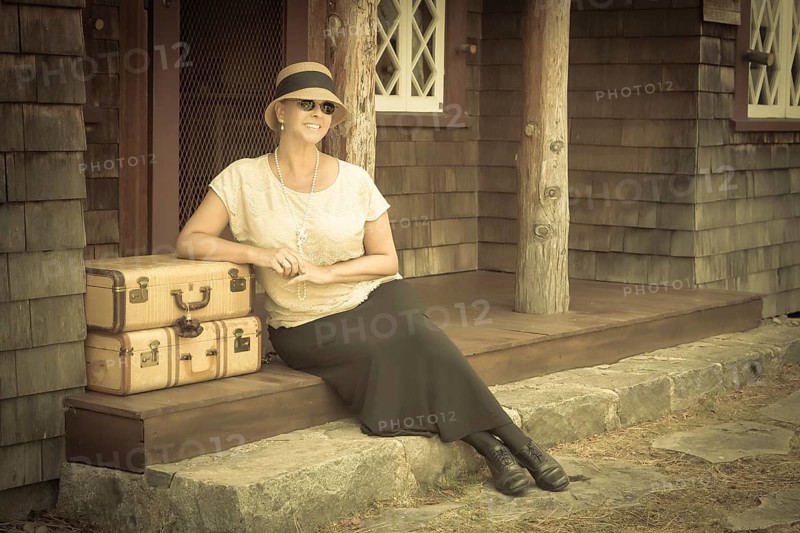 Pretty 1920s dressed girl next to suitcases on porch with vintage effect added