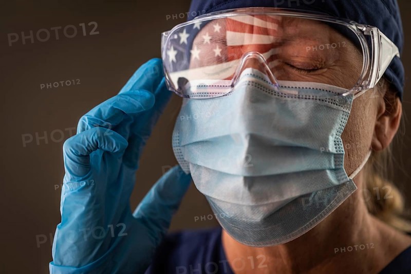 American flag reflecting on distressed female medical worker wearing protective face mask and goggles