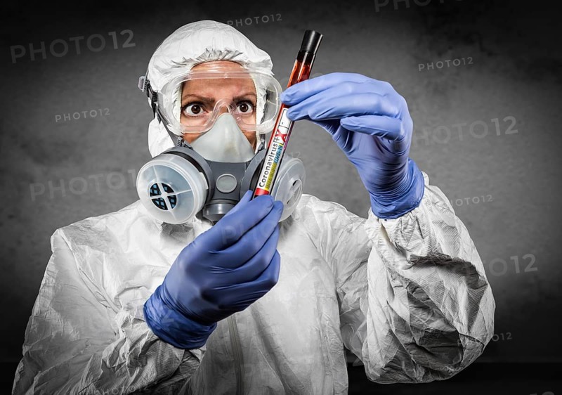 Female doctor or nurse in hazmat gear holding positive coronavirus test tube