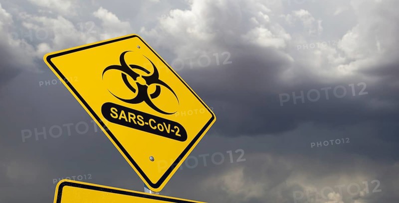 Bio-hazard symbol with sars-cov-2 coronaravirus yellow road sign against ominous stormy cloudy sky