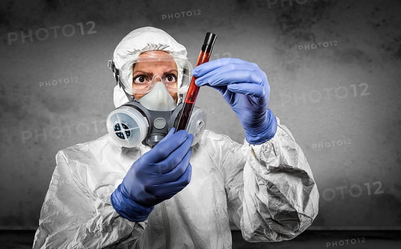 Woman in hazmat suit and gas mask holding test tube of blood in dark room
