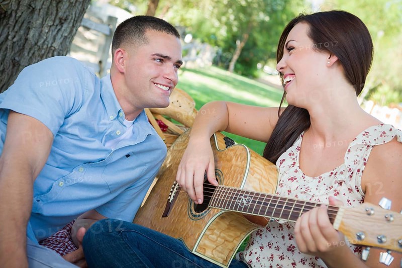 Happy mixed-race couple at the park playing guitar and singing songs