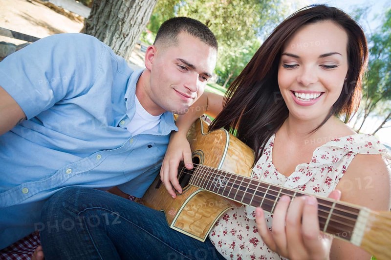 Happy mixed-race couple at the park playing guitar and singing songs