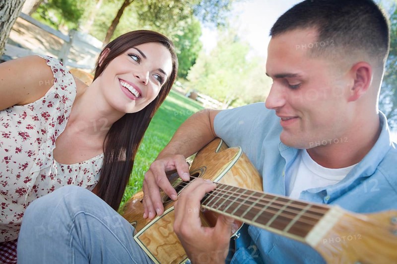 Happy mixed-race couple at the park playing guitar and singing songs