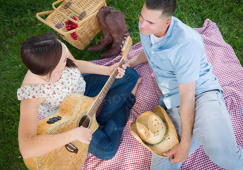 Happy mixed-race couple at the park playing guitar and singing songs