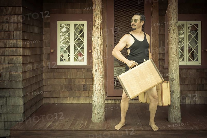 Goofy gentleman dressed in 1920's era swimsuit holding suitcases on porch of cabin