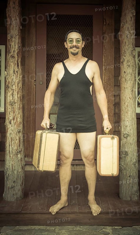 Goofy gentleman dressed in 1920's era swimsuit holding suitcases on porch of cabin